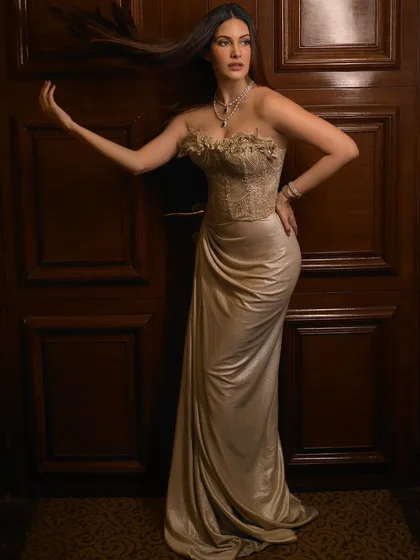 A full-length portrait of Amyra Dastur, with a sense of movement in her hair. The warm wood background adds a touch of classic elegance.