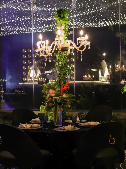An indoor-outdoor dining experience, with a table set against a large glass window that reflects the thousands of fairy lights from the ceiling.