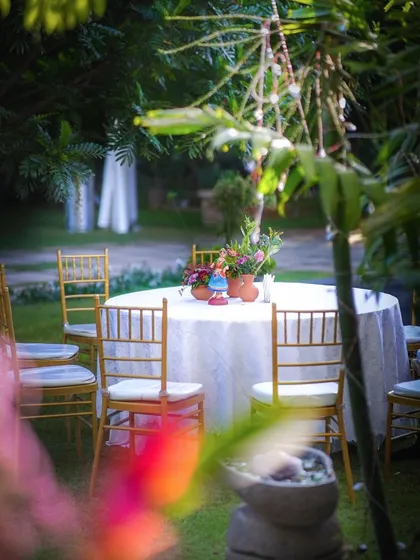 A simple table setting in a garden for a pre-wedding event, with a colorful Kondapalli doll as the centerpiece.