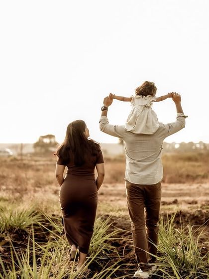A beautiful family walk into the sunset. The dad carries their daughter on his shoulders as they walk alongside the expectant mom, a perfect picture of their growing family.