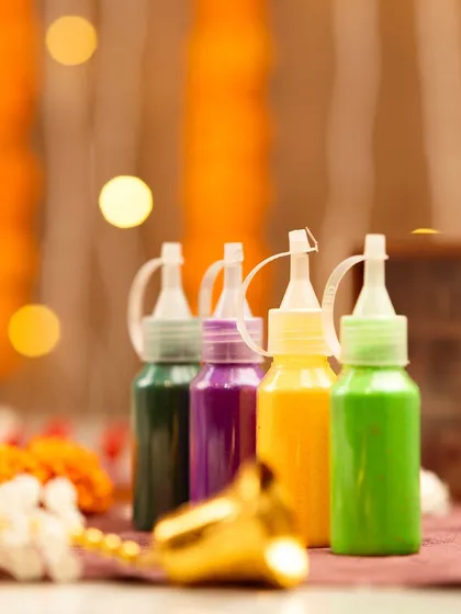 A close-up of colorful rangoli paint bottles with a beautiful bokeh background of festive lights.