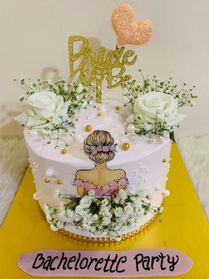A pretty bachelorette party cake with a "Bride to Be" theme, decorated with fresh baby's breath and a lovely illustration.