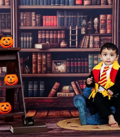 Ready to cast a spell. This portrait from a Harry Potter themed shoot shows the full setup, including the library backdrop and Halloween-inspired pumpkin props.