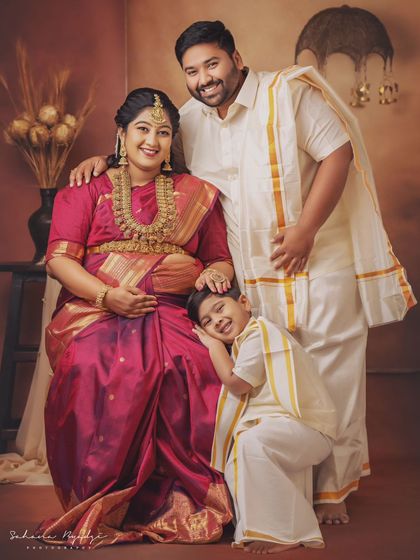 A complete family portrait glowing with happiness. The older brother gently rests his head on his mother's shoulder, a sweet moment captured during their traditional maternity photoshoot.