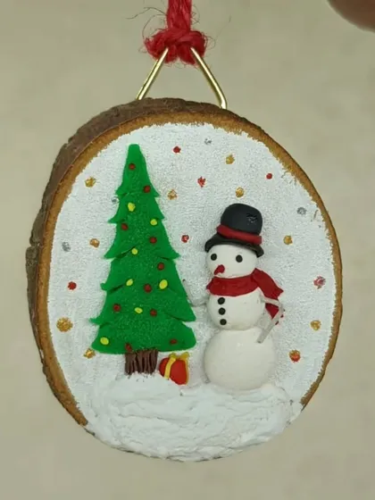 This Christmas ornament is made on a wood slice, featuring a snowman and a tree in a snowy scene.