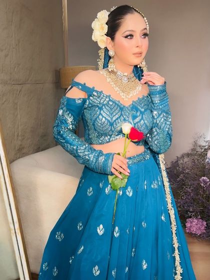 A model in a beautiful teal blue lehenga with cold-shoulder sleeves, perfect for a sangeet or reception.