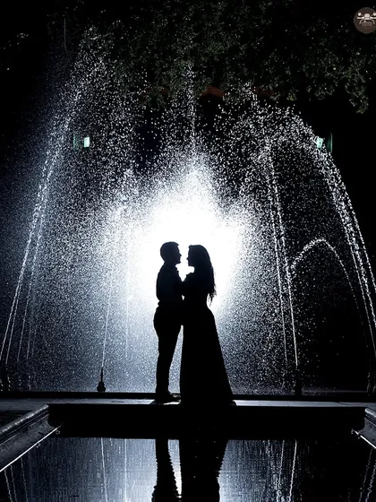A dramatic silhouette shot against a backlit fountain at night. This type of creative portraiture uses light and shadow to create artistic and powerful images that stand out in any pre-wedding collection.