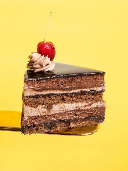 A perfect slice of my eggless Chocolate Mousse Cake against a vibrant yellow background. You can see the distinct, fluffy layers of milk and dark chocolate mousse.