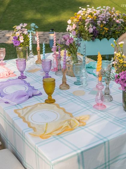A dining table set with a checkered cloth, colorful glassware, and whimsical twisted candles, completing the playful French picnic look.