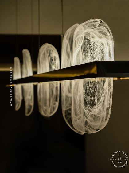 This linear pendant features organic, rounded glass elements with a beautiful white smoke effect inside. Suspended from a simple gold bar, it provides a soft, ethereal glow, ideal for creating a serene atmosphere over a dining table.