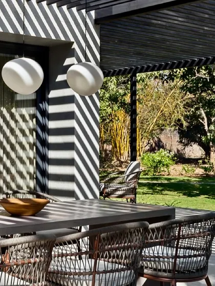 A detail of the outdoor dining area, showing how the spherical pendant lights add a soft, sculptural element that contrasts with the linear shadows from the pergola.
