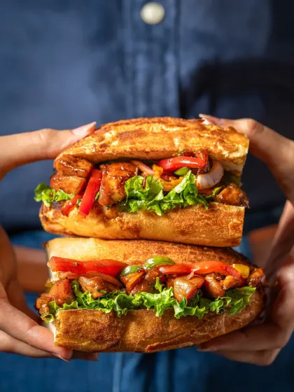 A hand-held shot of a loaded chicken sandwich, cut in half to show the generous filling of chicken, peppers, and lettuce.