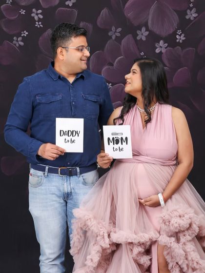 A classic studio announcement portrait. The couple sits together holding "Mom to be" and "Daddy to be" signs, looking at each other with love and excitement.