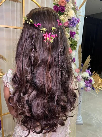 A bohemian-inspired hairstyle with loose curls, small braids, and delicate fresh flowers, perfect for a relaxed and romantic vibe.
