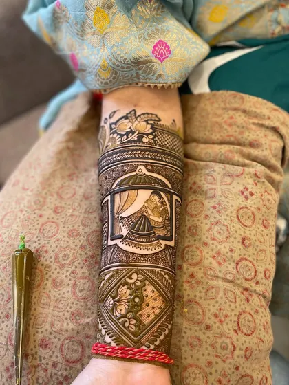 A full view of an intricate arm design, showing the mehndi cone I use. The design features a bride portrait, lotus patterns, and geometric fills.