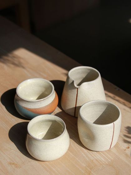 A minimalist and elegant collection of white and cream colored pieces, including a pitcher and small bowls with subtle line details.