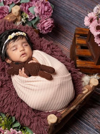 Another angle from the floral bed setup, this time showing the baby sleeping peacefully with a teddy bear. This view highlights the full arrangement of props and flowers that create the magical scene.