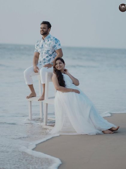 A serene portrait of the couple by the water's edge. The soft whites of their outfits and the gentle waves create a peaceful and romantic mood.