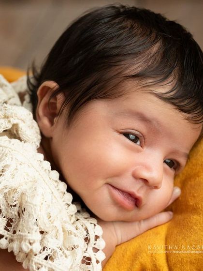 A one-month-old baby girl gives a sweet smile from her cozy spot on a yellow pillow. Her personality is just beginning to blossom in this happy portrait.