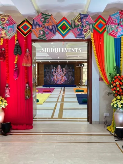 A vibrant entrance for a festive celebration, using colorful Gujarati umbrellas, traditional dolls, and bright floral arrangements to welcome guests to the event.