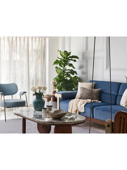 The living room features a soothing color palette with a plush blue sofa and a custom lounge chair. The space is designed to feel relaxed and structured, with classical wall mouldings adding a touch of elegance.