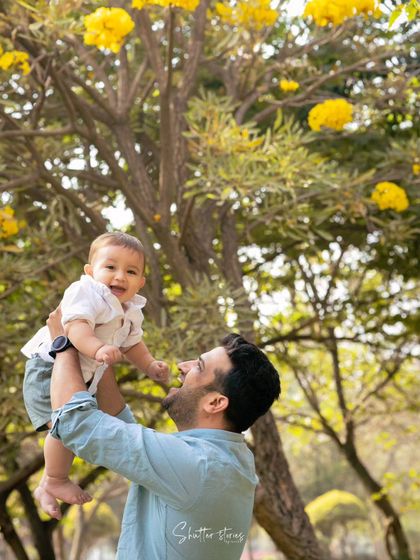A father joyfully lifts his baby boy up in the air, both of them smiling from ear to ear.