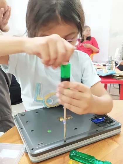 A young girl carefully uses a screwdriver to open up a digital weighing scale. Our workshops empower kids to fearlessly investigate how things work, turning curiosity into practical knowledge.
