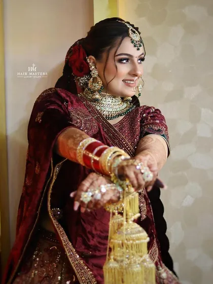 A joyful bride in a deep maroon velvet lehenga. Her makeup is glamorous yet elegant, with a red rose in her hair adding a touch of romance.