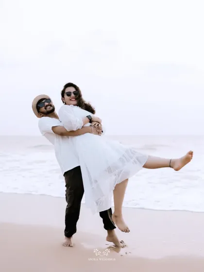 A playful and joyful moment, with the groom lifting the bride up on the beach.