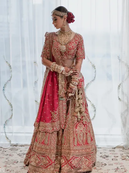 A classic full-length portrait of the bride in her magnificent red and gold lehenga, radiating timeless elegance.