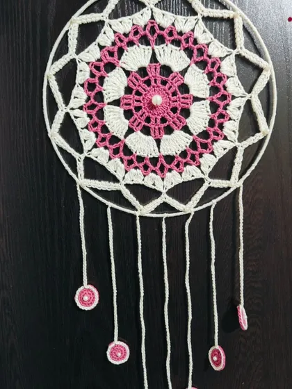 A full view of the pink and white dreamcatcher, showing the delicate hanging threads with small crocheted circles. A perfect piece for a serene bedroom.