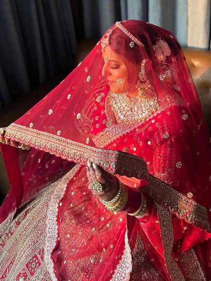 A beautiful bride on her wedding day, with her hair in a classic floral bun, peeking from under her red veil.