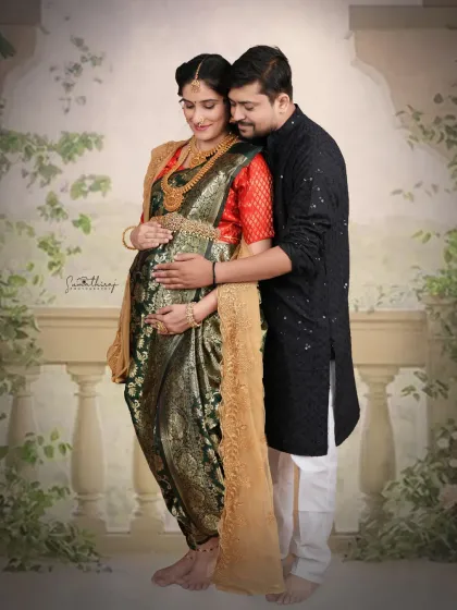 A beautiful standing portrait of a couple in traditional attire. The husband's hands gently cradle his wife's baby bump, creating a classic and loving maternity image.