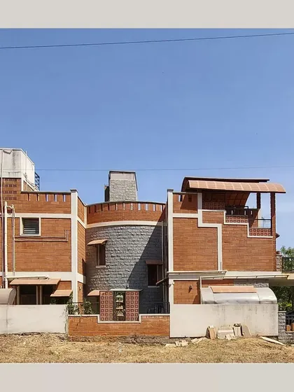 A view of the Lakshmi and Praveen residence, highlighting its cylindrical stone-clad tower and the clean lines of the exposed brickwork against a clear blue sky.
