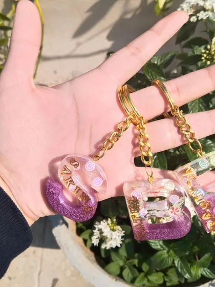My custom initial keychains are perfect for gifting or for yourself. Here you can see a set made for a group, each with a unique name and color combination. I can personalize these with different colors, glitters, and names.