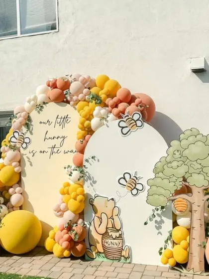 Our classic Winnie the Pooh baby shower theme, "Our Little Hunny is on the way". This outdoor setup brings the Hundred Acre Wood to life with custom character cutouts, themed backdrops, and a cheerful balloon arch in shades of yellow, orange, and cream.