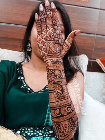 A happy client posing with her intricate bridal mehandi. The design covers her full arm, featuring a mix of traditional Indian art forms and patterns.