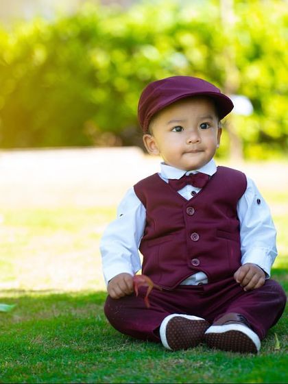 A relaxed and happy portrait of a one-year-old boy sitting in the grass. Outdoor sessions allow for natural, unposed moments like this.