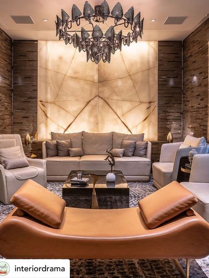 This living room, featured by Interior Drama, showcases an onyx backdrop that adds a significant luxe quotient. The backlit natural stone becomes the focal point, complemented by a sculptural chandelier and a mix of leather and fabric seating.