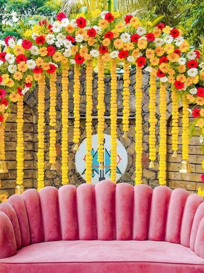 A vibrant haldi or baby shower backdrop with an arch of yellow, orange, and white gerbera daisies and hanging marigold strings.