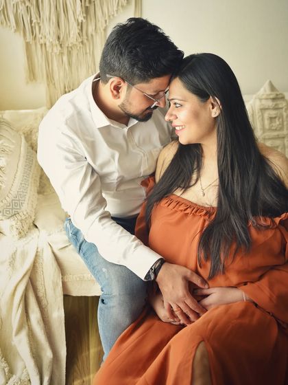 An intimate portrait of a couple in a cozy, rustic setting. The warm tones of the off-the-shoulder dress and the gentle embrace make this a very romantic maternity photo.