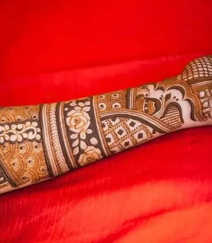 A close up of a forearm, showing a band of delicate rose patterns combined with traditional jaali work.