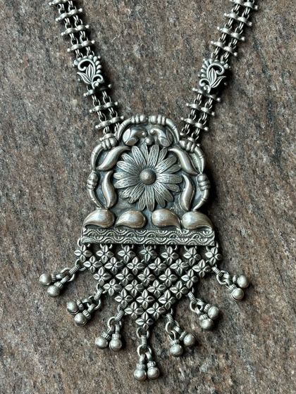A close-up of an antique oxidised silver pendant. The floral design is incredibly detailed, showcasing the skill of our artisans.