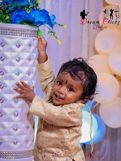 A playful moment during a baby's birthday shoot. He is caught looking at the camera with a cheeky grin while holding onto a large decorative vase.