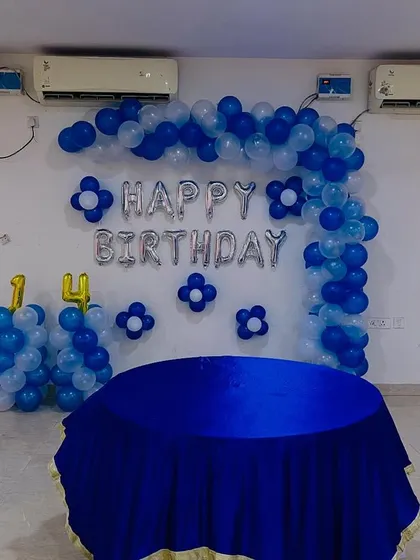 Here is a complete birthday backdrop setup for a 14th birthday. It includes a half-arch of blue and white balloons, "Happy Birthday" foil letters, and balloon pillars with the number '14'.
