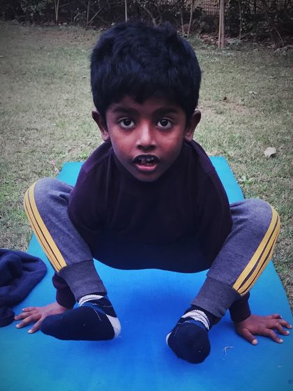 A little boy masters Lolasana, the pendant pose, showing great strength and concentration.