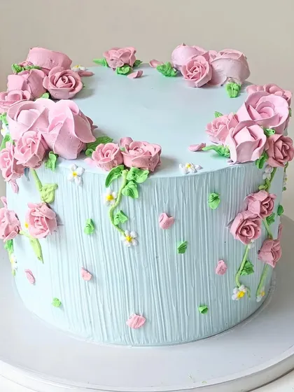 A charming blue cake covered in hand-piped pink buttercream roses. The textured vertical lines on the cake add another layer of detail to this floral design.