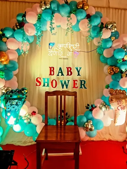 A traditional Marathi baby shower, also known as 'dohale jevan'. The setup includes a circular balloon arch and a special chair for the mother-to-be, with a sign that reads "Kunitari yenar ga" (Somebody's coming).