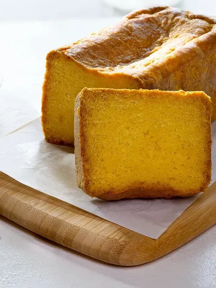 A slice of golden tea cake on a wooden board. The simple, bright styling gives it a light and airy feel, perfect for an afternoon snack.