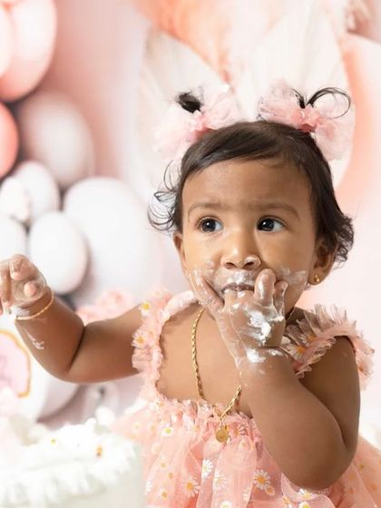 A sweet one-year-old girl enjoying her pink-themed cake smash session. I love capturing these close-ups of their frosting-covered fingers and happy faces.